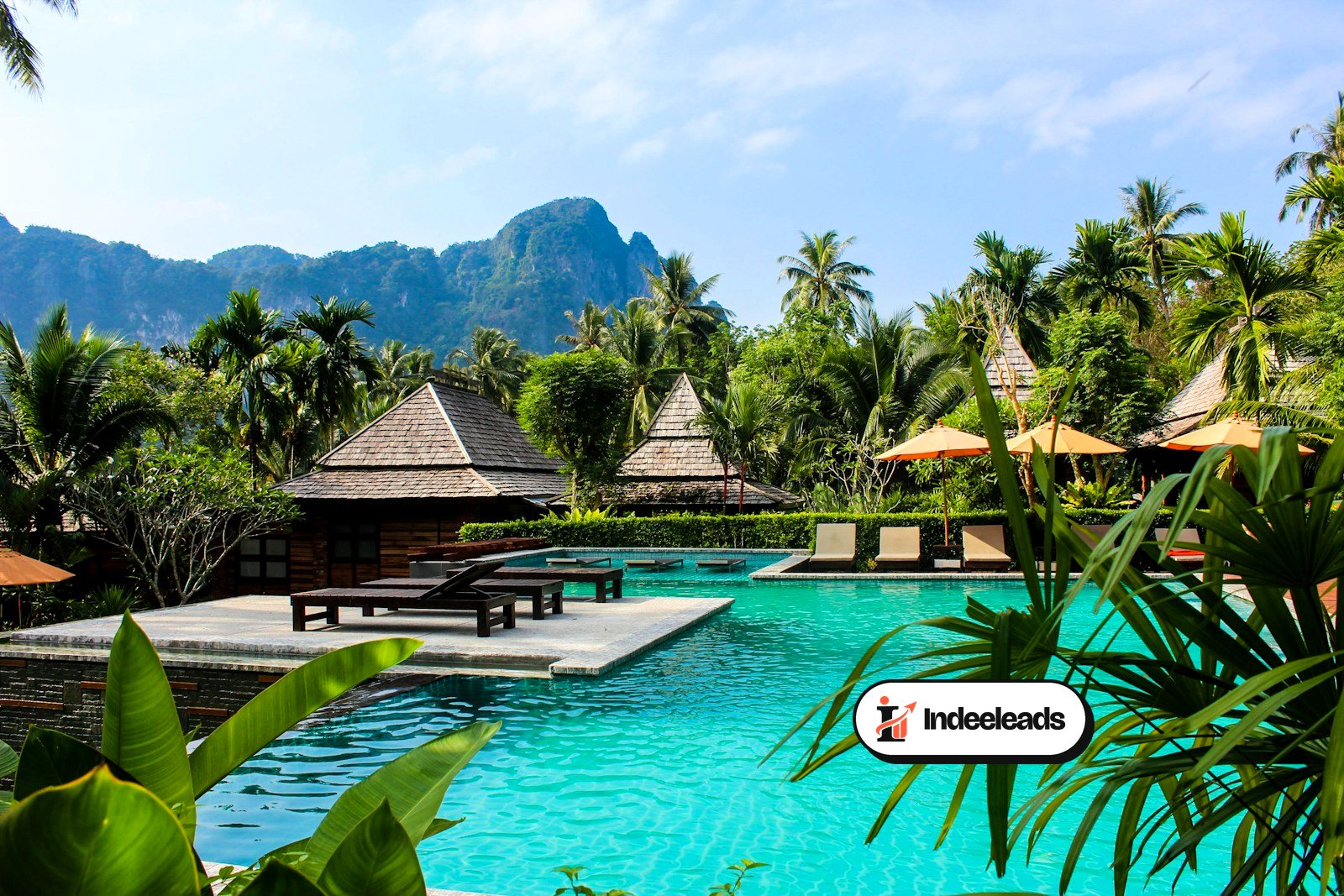 Tropical resort pool with thatched villas and mountains behind